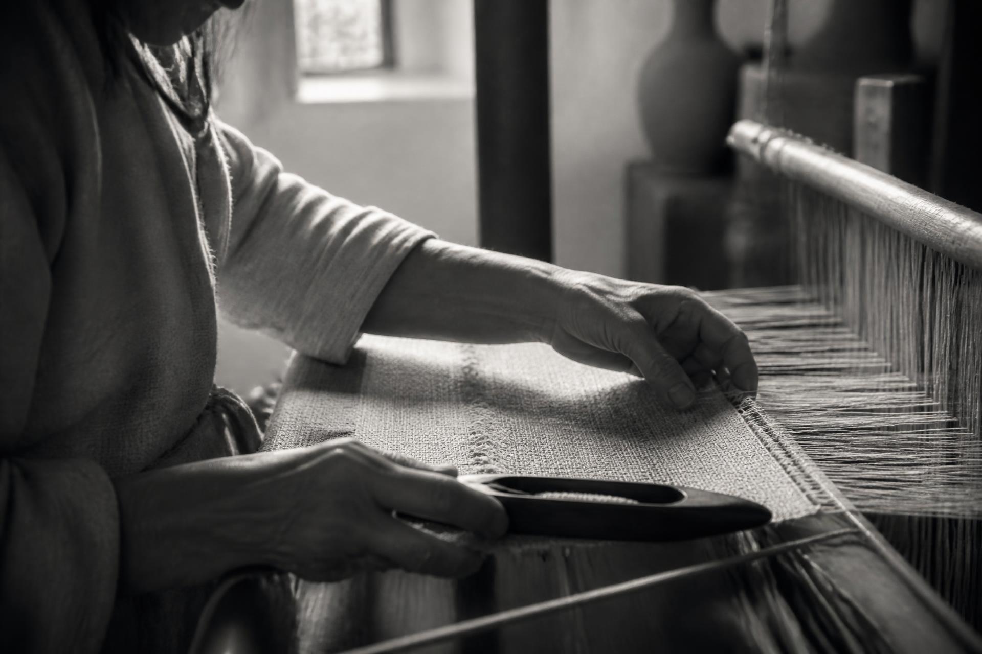 Hands weaving linen on a wooden loom in soft window light